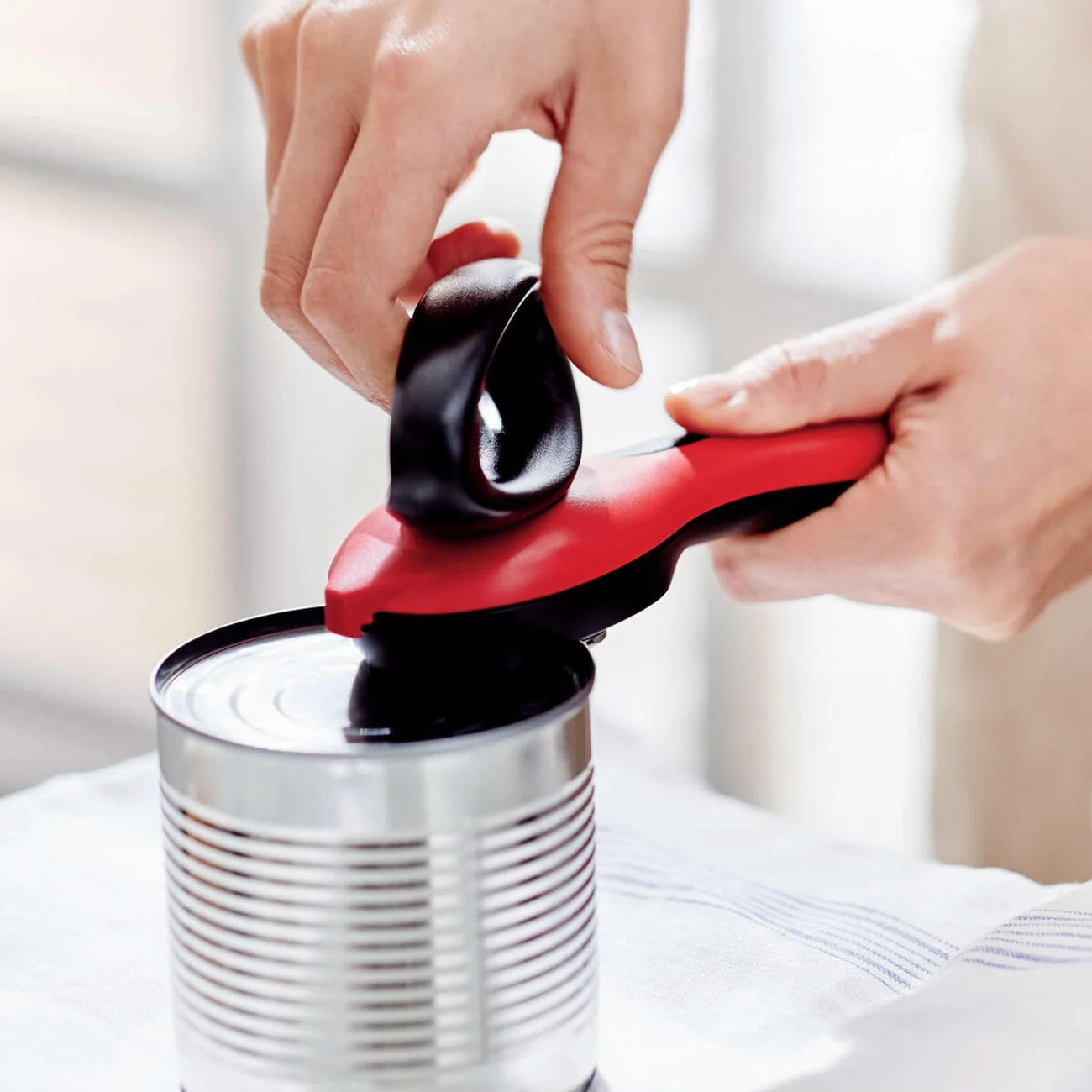 Dosenöffner von der Marke Tupperware in der Farbe Rot / mit sicherem Mechanismus gegen Scharfe Kanten / Einfach und Solide / sorgt für abgerundete Schnittkanten / Komfort dank ergonomisch geformten Griff / mit Greifer zum abnehmen des Abgeschnittenen Deckels / Beispielbild Öffner beim Dosenöffnen / Hier direkt online kaufen 
